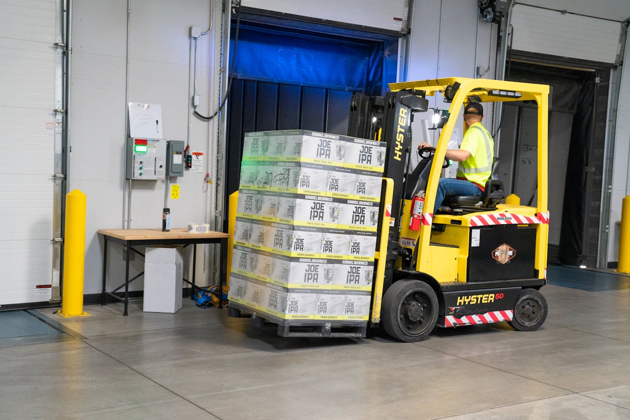 services-02 A warehouse employee operating a forklift to move stocked goods indoors. Perfect for industry and logistics visuals.