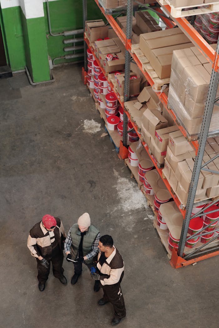 services-04 Group of warehouse workers discussing logistics and inventory in a large storage area with shelves and packages.