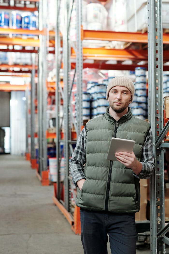 services-01 Man wearing beanie holds tablet in industrial warehouse setting.
