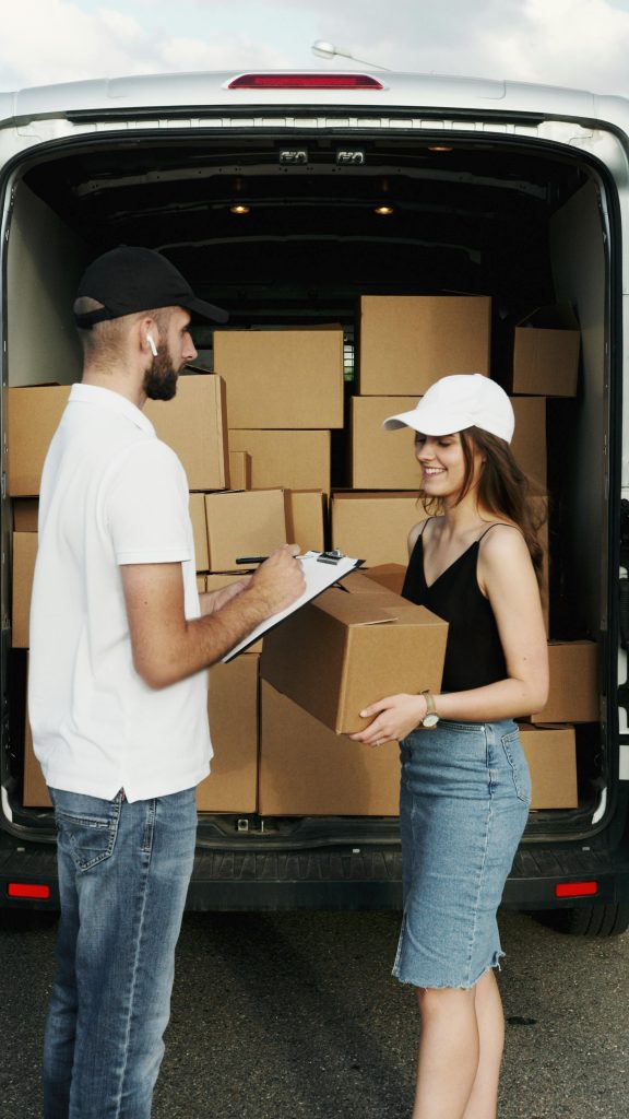 pexels photo 5025502 5025502 A delivery person hands a package to a woman from a van full of parcels outdoors.